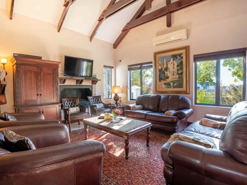 Spacious living room featuring a high vaulted ceiling with exposed timber beams, a cozy fireplace, and large windows providing natural light.