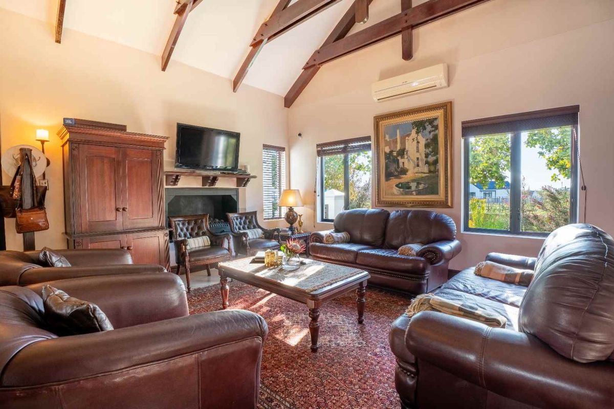 Spacious living room featuring a high vaulted ceiling with exposed timber beams, a cozy fireplace, and large windows providing natural light.