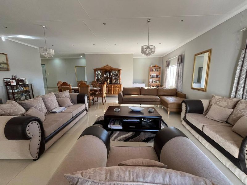 Spacious open-plan living and dining area featuring neutral tiled flooring, recessed downlighting, and elegant crystal chandeliers in a well-maintained interior space.