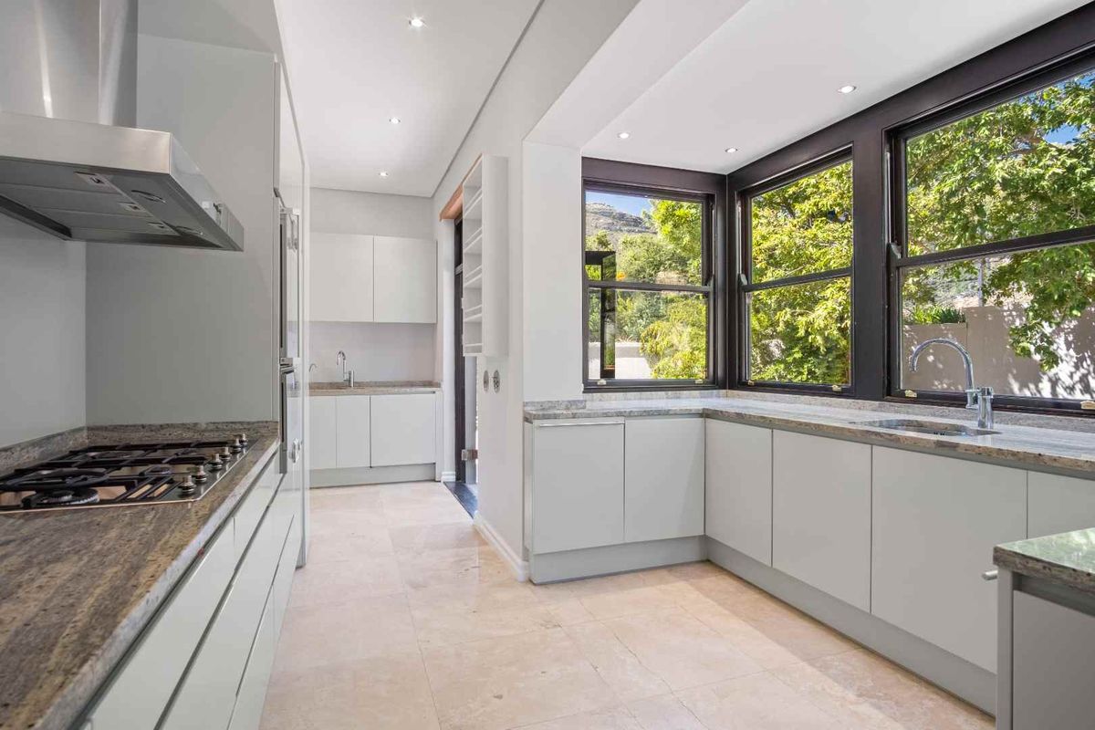 Modern kitchen featuring stone countertops, gas cooktop, stainless steel extractor, and ample cabinetry with large windows overlooking the garden.