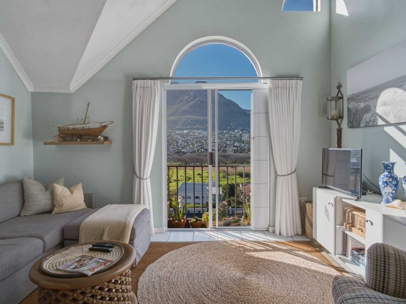 A bright living room featuring a vaulted ceiling, arched window, and sliding glass door leading to a balcony with scenic mountain and landscape views.