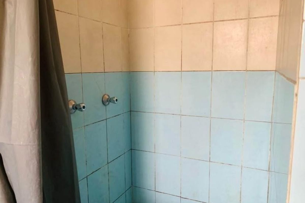 A dated shower enclosure featuring two-tone blue and cream ceramic wall tiles and standard shower plumbing fixtures.