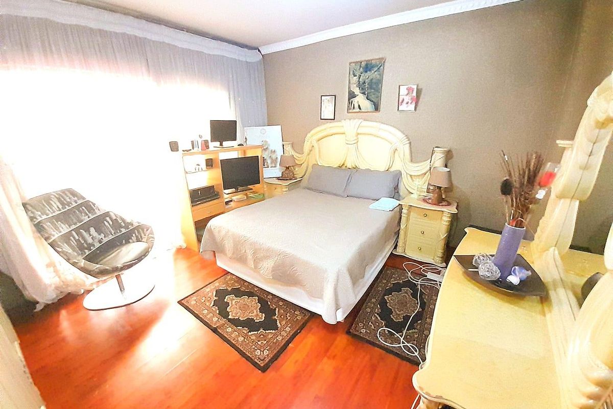 A bedroom featuring warm-toned wooden flooring, crown molding, and large windows allowing for ample natural light.
