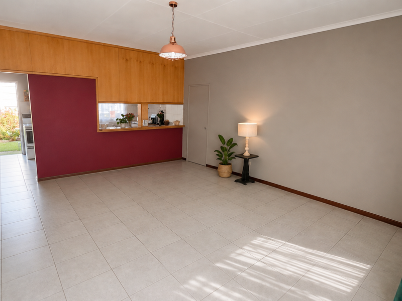 Spacious open-plan living area featuring neutral tiled flooring, a pass-through kitchen window, and built-in wooden cabinetry, offering a versatile layout.