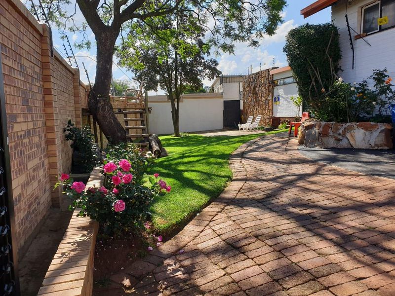 A well-maintained rear garden featuring brick paving, a stone-clad retaining wall, and established trees, enclosed by a brick boundary wall with electric fencing.