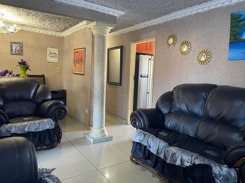 Living room featuring ceramic floor tiles, a decorative structural column, and textured ceilings with crown molding, leading into an adjacent kitchen area.