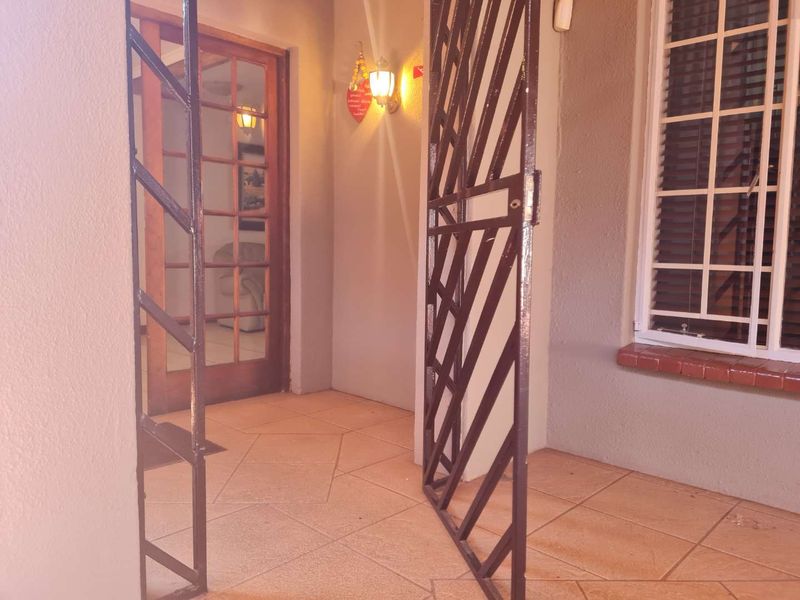 A covered entrance area featuring tiled flooring, a secure metal gate, and a timber-framed glass door leading into the home.