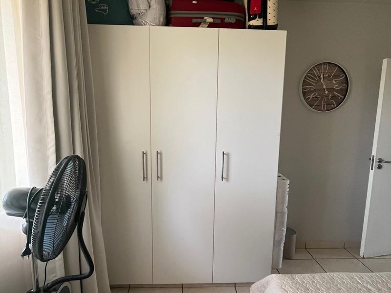 A bedroom featuring a white built-in wardrobe and neutral tiled flooring, providing functional storage space within the room.