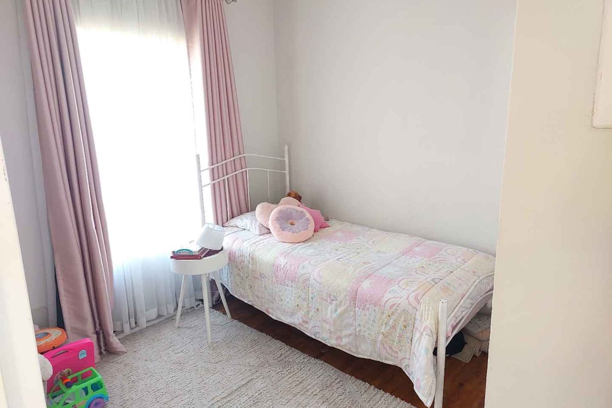 A compact bedroom featuring laminate flooring and large window with curtain tracks, providing natural light.