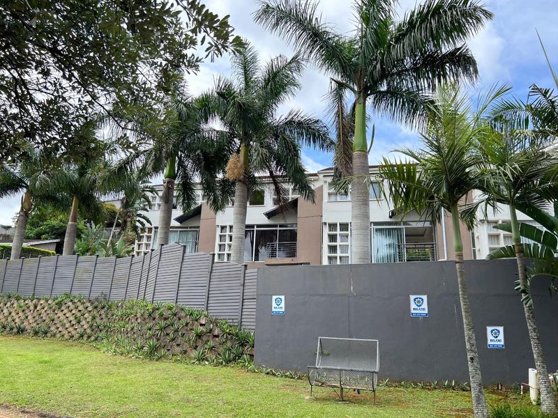 Rear elevation of a multi-story cluster home featuring balconies, sliding doors, and a well-maintained garden with perimeter fencing.
