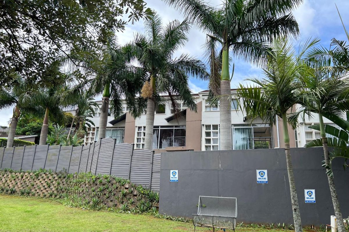 Rear elevation of a multi-story cluster home featuring balconies, sliding doors, and a well-maintained garden with perimeter fencing.