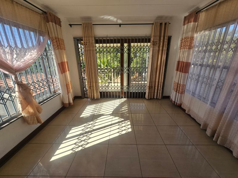 A bright, empty living room featuring tiled flooring, security gates on windows and doors, and direct access to an outdoor area.