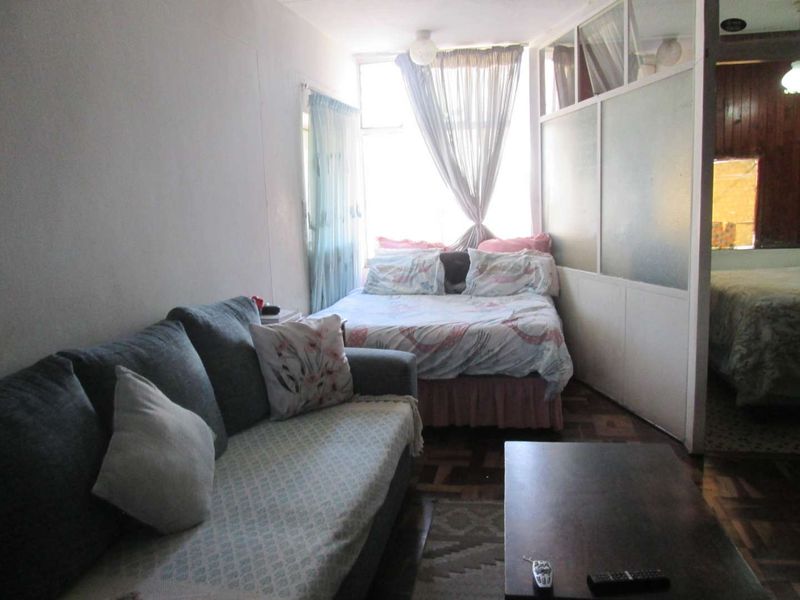 A compact bedroom featuring parquet flooring and a semi-private partition wall, offering a functional layout with natural light from the window.