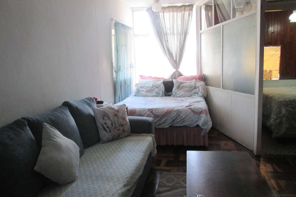 A compact bedroom featuring parquet flooring and a semi-private partition wall, offering a functional layout with natural light from the window.