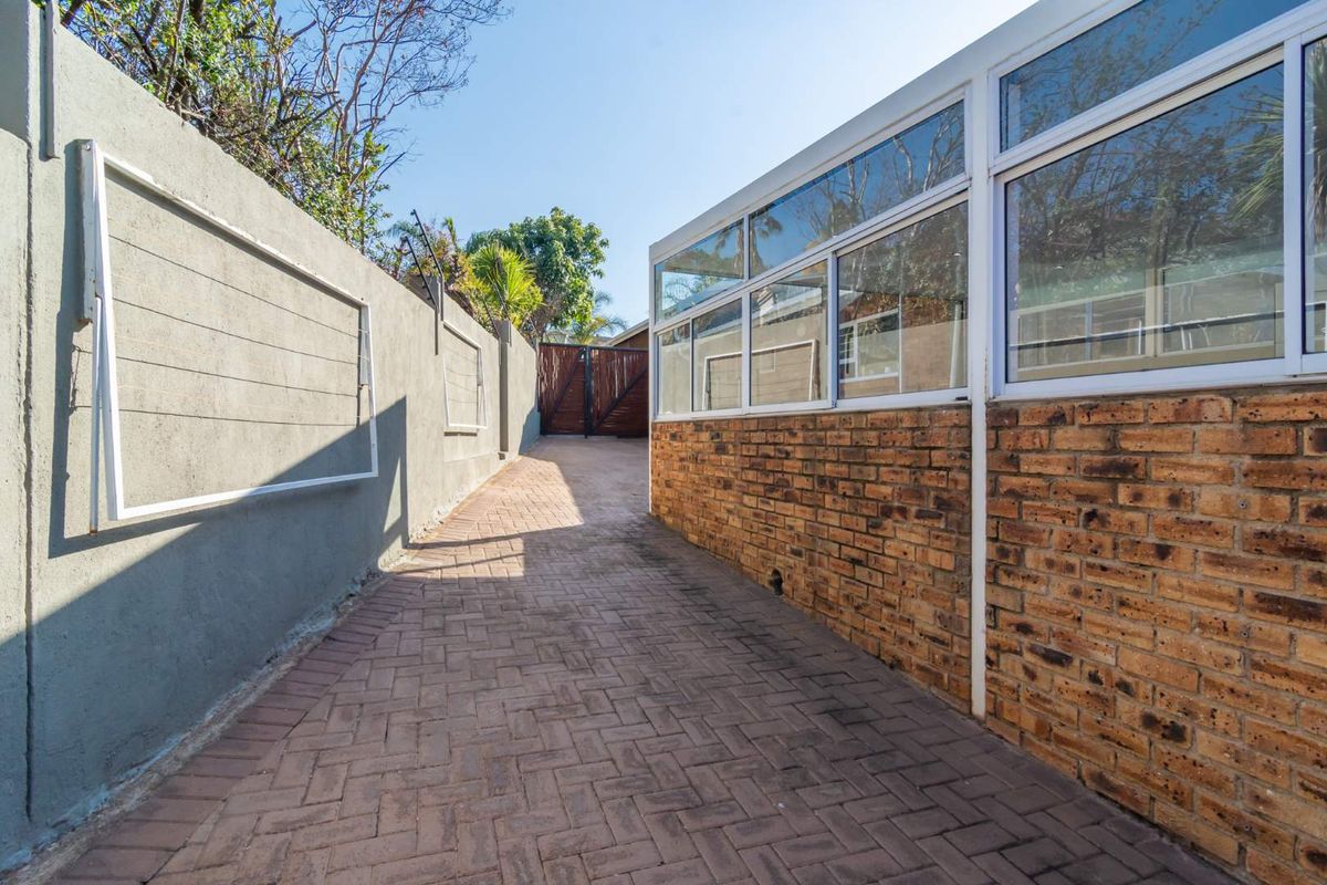 A side walkway featuring brick paving, a solid boundary wall, and an exterior wall with large aluminium-framed windows.