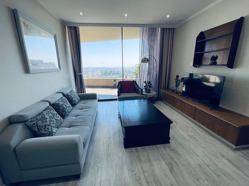 A bright living room featuring modern laminate flooring, recessed lighting, and a large sliding glass door providing access to a balcony with expansive views.
