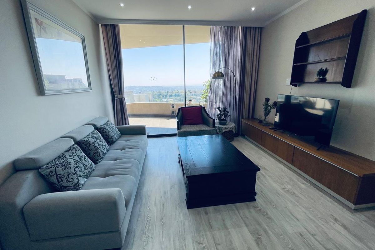 A bright living room featuring modern laminate flooring, recessed lighting, and a large sliding glass door providing access to a balcony with expansive views.