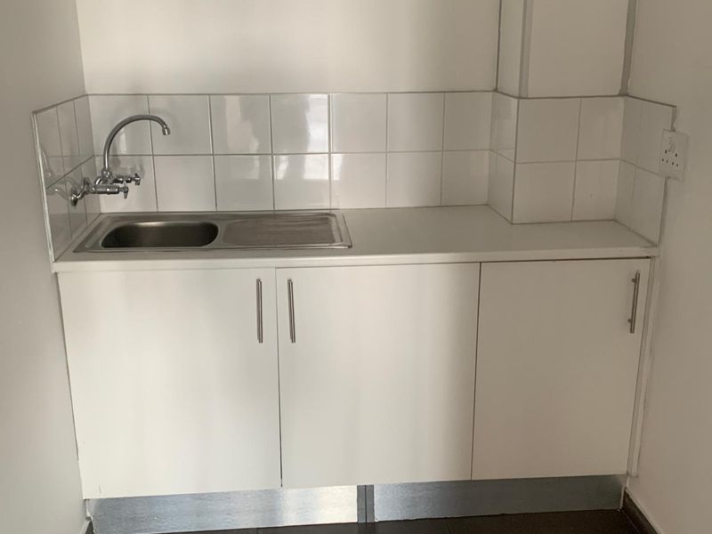 A compact kitchenette area featuring white built-in cabinetry, a stainless steel sink, and a tiled backsplash.