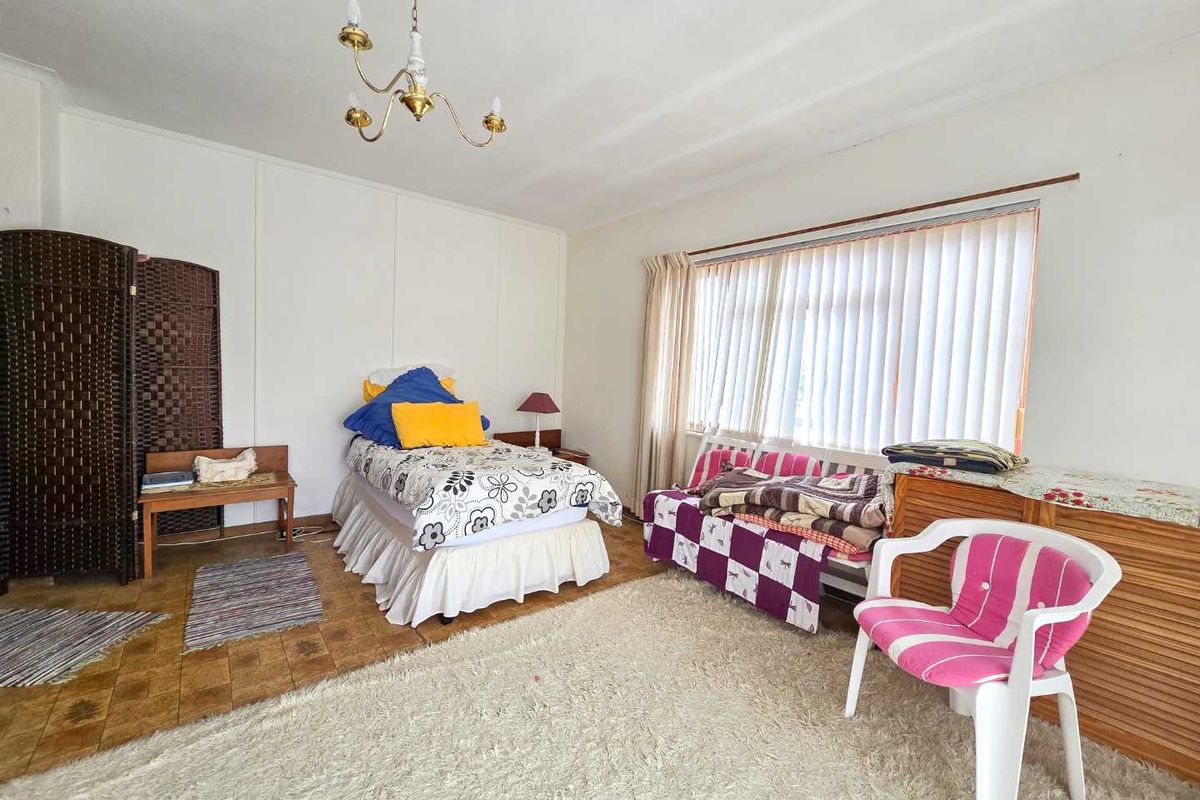 A spacious bedroom featuring large windows with vertical blinds, tiled flooring, and a classic chandelier fixture.