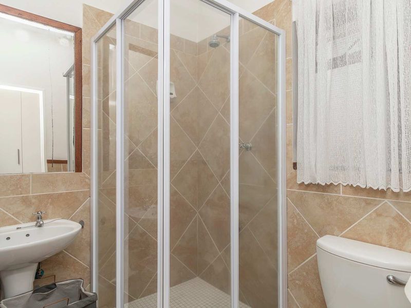 A functional bathroom featuring a corner shower enclosure, pedestal basin, and toilet with neutral wall tiling.