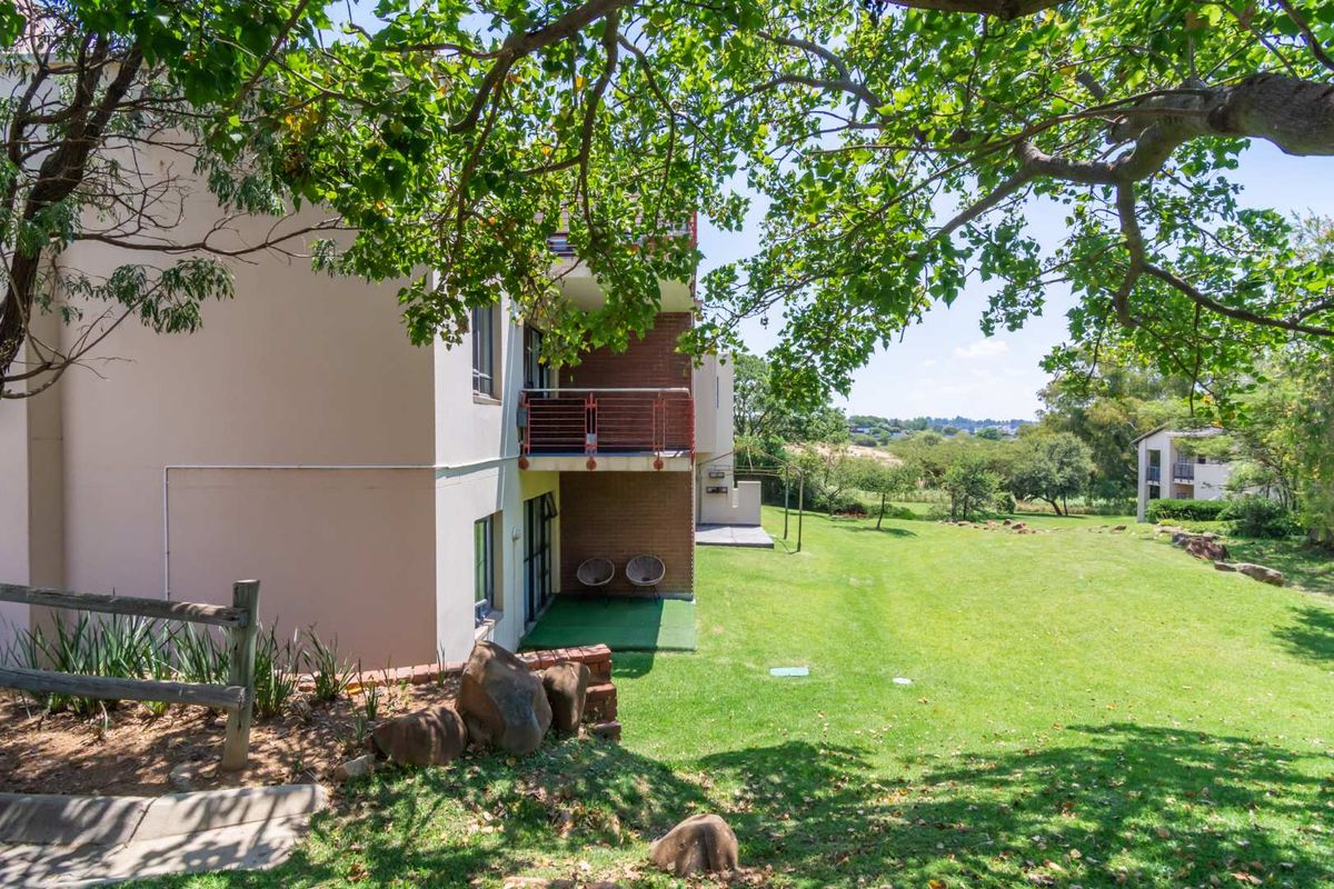 Exterior view of the apartment building featuring a ground floor patio area, balcony above, and expansive communal garden space.