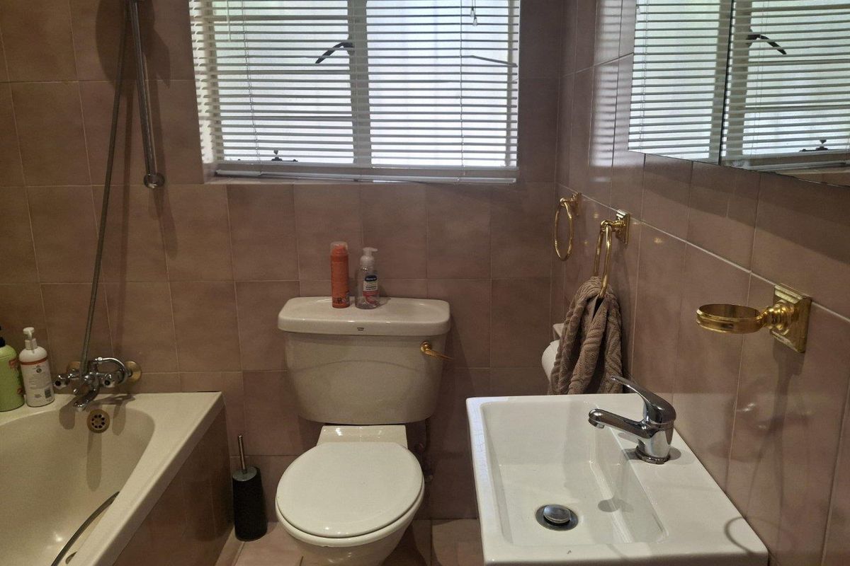 A functional bathroom featuring a bathtub, toilet, and wall-mounted basin with tiled finishes and natural light from a window.