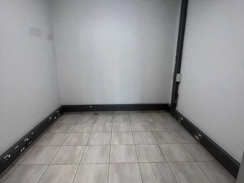 A vacant office space featuring tiled flooring, surface-mounted electrical trunking, and a standard fluorescent light fixture.