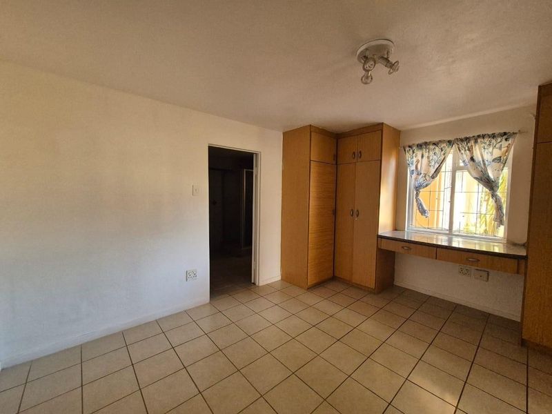 A vacant bedroom featuring built-in wooden cupboards, a built-in desk, tiled flooring, and security bars on the window.