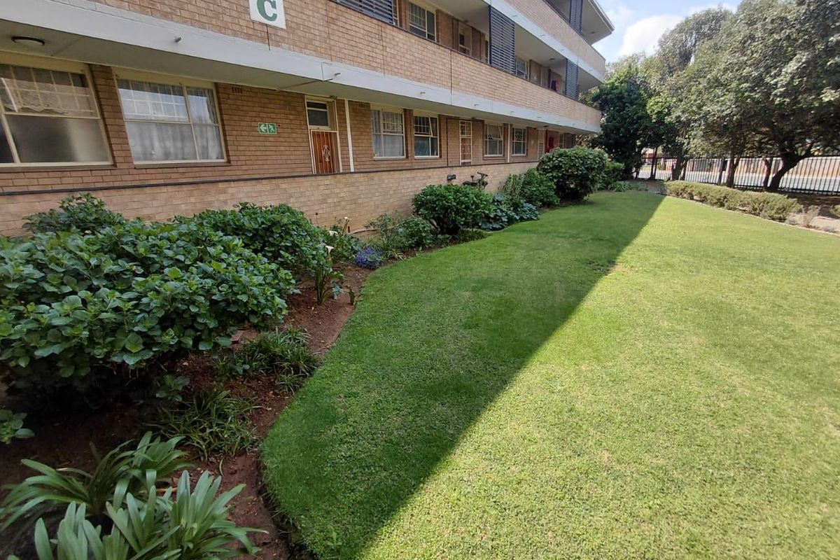 A view of the rear exterior of a brick apartment building featuring a well-maintained lawn and landscaped garden area.
