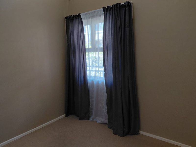 A vacant bedroom featuring neutral wall paint, carpeted flooring, and a window with installed curtain tracks.