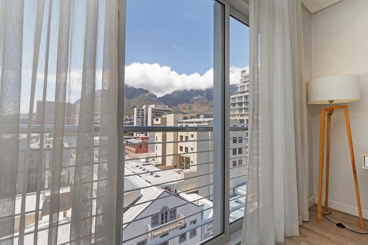 A clear view of the city skyline and mountain range from an apartment balcony with sliding glass doors and modern flooring.