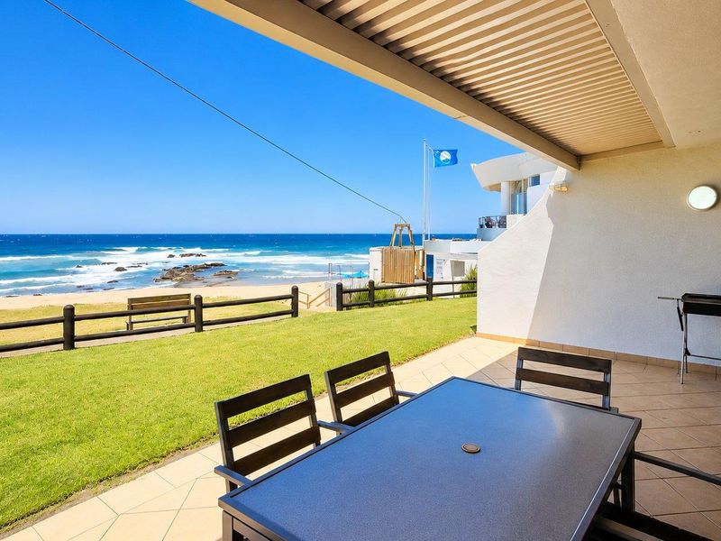 A spacious covered patio featuring tiled flooring and direct access to a lawn area with stunning ocean views.