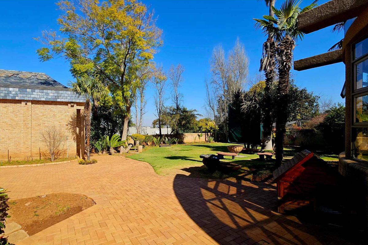 Spacious rear garden featuring a paved patio area, established trees, and a well-maintained lawn, providing a private outdoor space for relaxation.