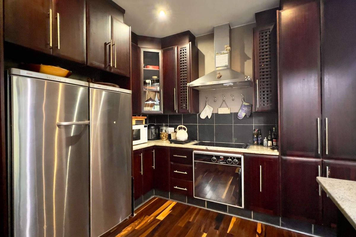 A functional kitchen featuring dark wood cabinetry, granite countertops, a built-in oven, extractor fan, and dark tiled backsplash with hardwood flooring.