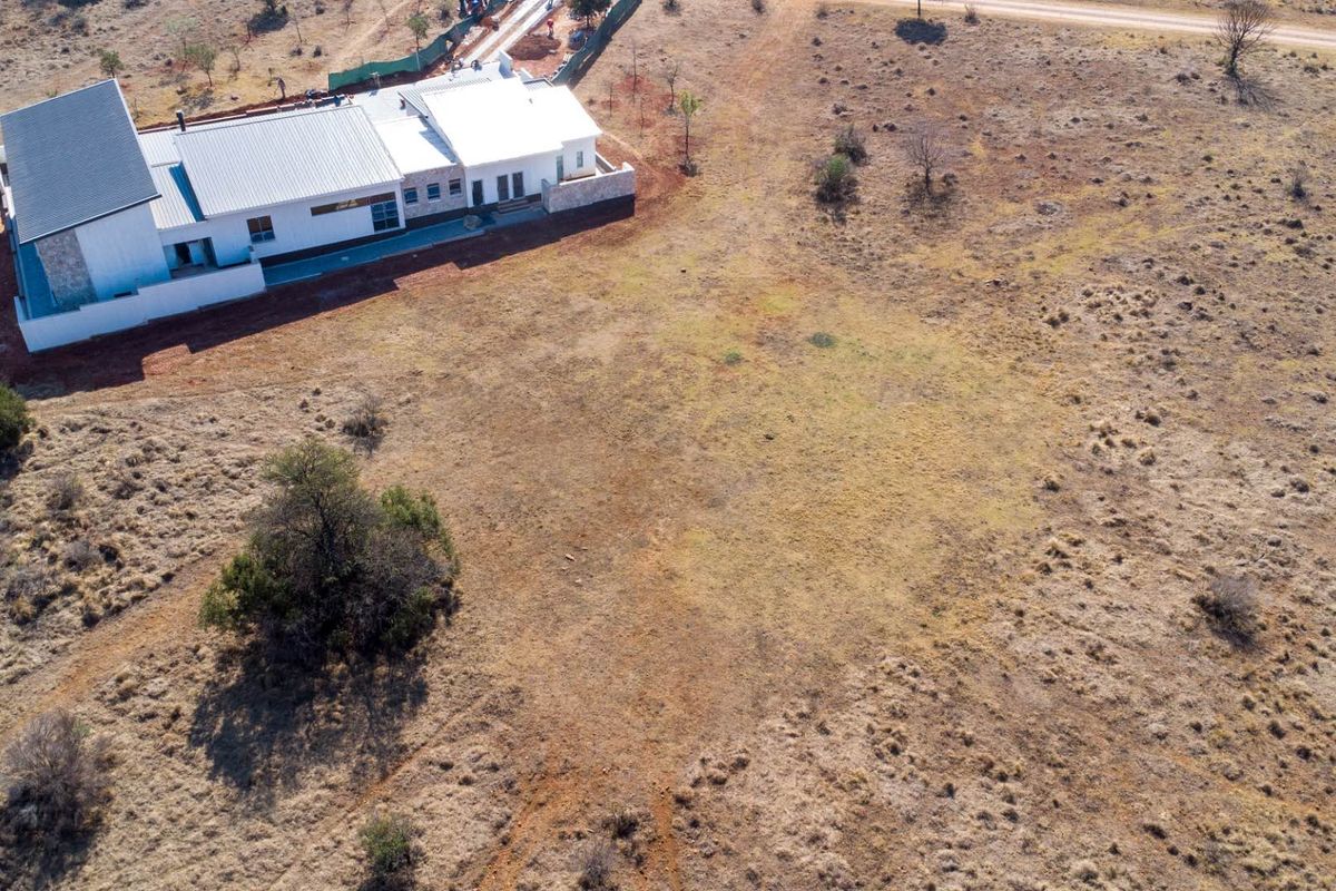 Aerial view of a residential property featuring a modern dwelling with a metal roof and stone cladding situated on a large vacant plot.