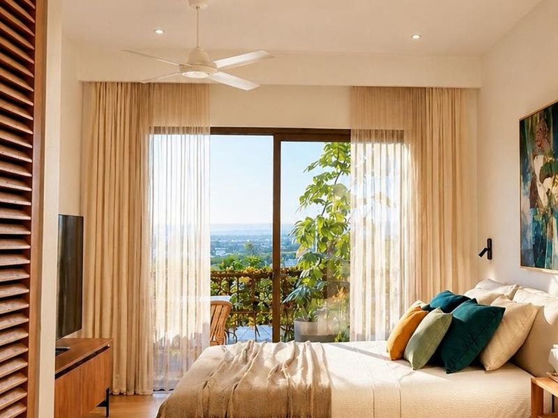 A bright, modern bedroom featuring light wood flooring, recessed ceiling lighting, a ceiling fan, and large sliding glass doors opening to a private balcony.