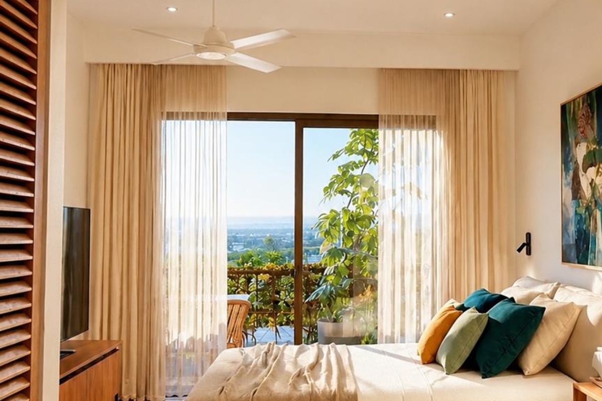 A bright, modern bedroom featuring light wood flooring, recessed ceiling lighting, a ceiling fan, and large sliding glass doors opening to a private balcony.