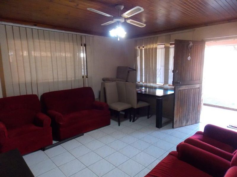 Living room featuring tiled flooring, a timber ceiling with a central fan, and vertical blinds, providing a dated but functional living space.