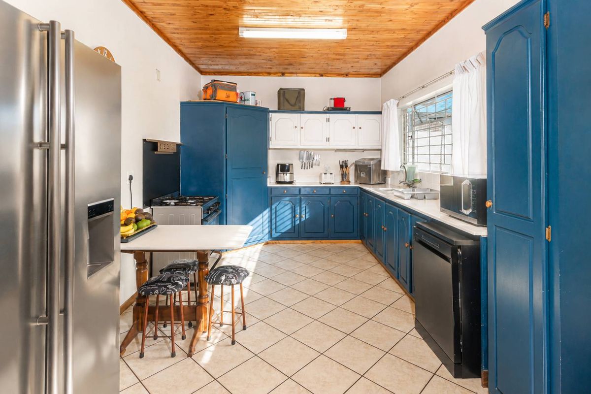 A functional kitchen featuring blue and white cabinetry, tiled flooring, and a timber-clad ceiling, offering ample storage and workspace.