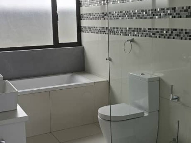 Modern bathroom featuring a built-in bathtub, glass-enclosed shower area, wall-mounted toilet, and contemporary mosaic tile accents with high-gloss floor tiles.
