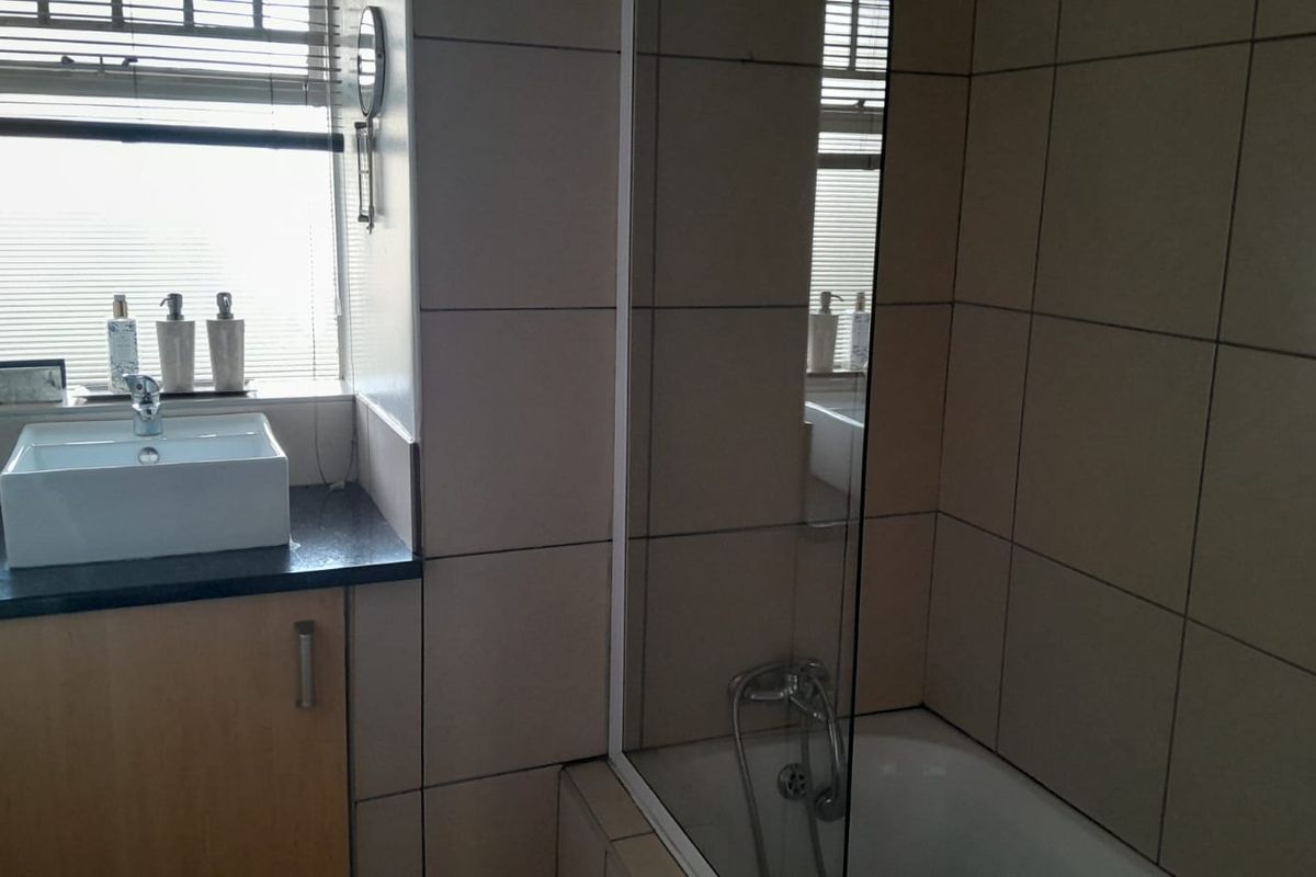 A functional bathroom featuring a vessel sink on a granite vanity, a bathtub with a glass shower screen, and neutral wall tiling.