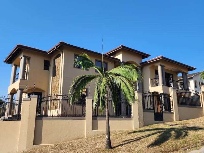 A modern double-story house featuring stone cladding, wrought iron fencing with electric security, and a tiled roof, viewed from the street.