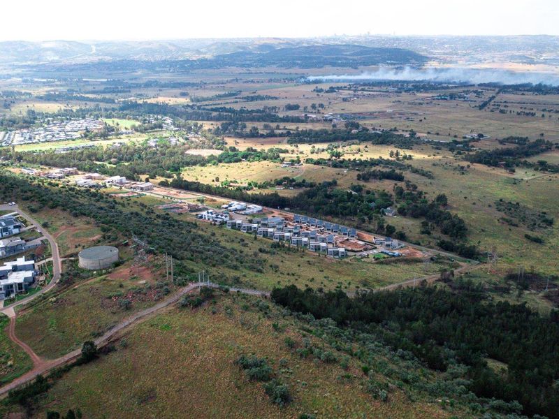 An aerial view of a residential estate development situated within a vast landscape, featuring access roads, utility infrastructure, and surrounding natural terrain.
