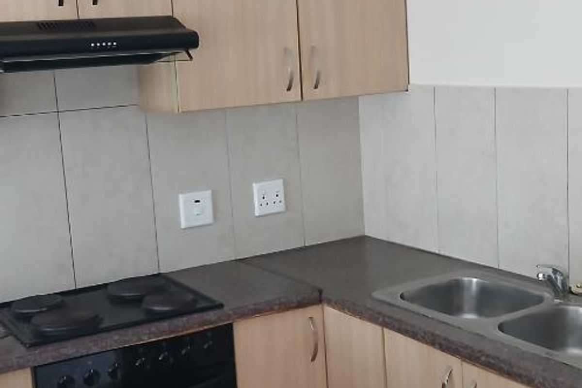 Compact kitchen featuring light wood-finish cabinetry, a built-in oven, electric hob, extractor fan, and a double stainless steel sink with tiled splashbacks.
