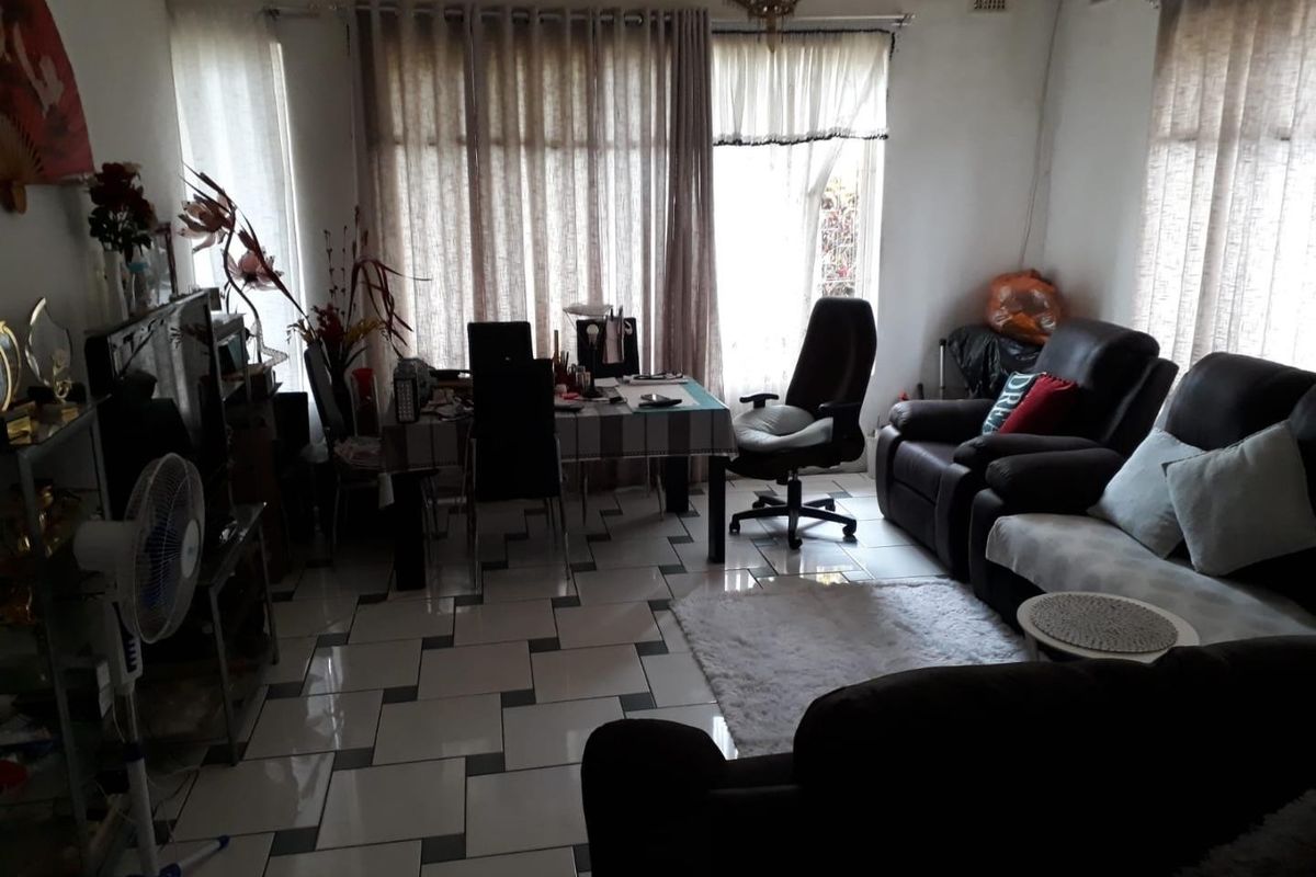 A living room area featuring tiled flooring and large windows, providing a functional space that could benefit from modern updates and improved lighting.
