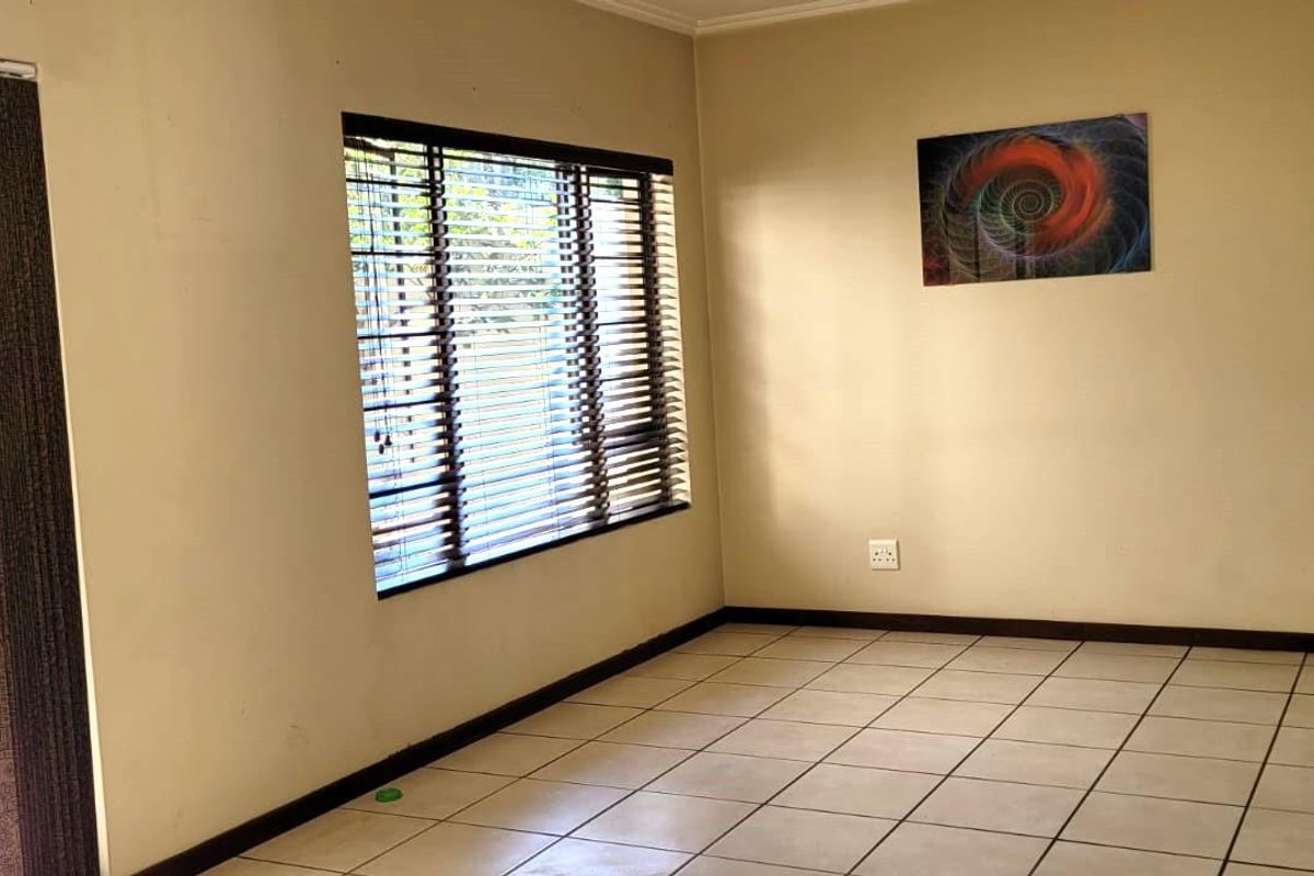 A bright, open-plan living area featuring neutral tiled flooring, large windows with venetian blinds, and direct access to an outdoor patio space.