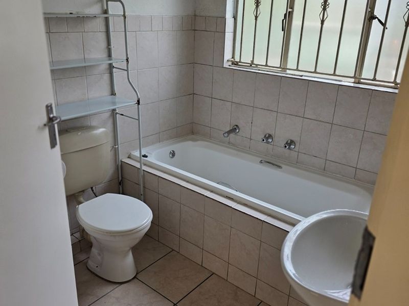 A dated bathroom featuring a bathtub, pedestal basin, and toilet, with tiled finishes and security bars on the window. Requires cosmetic updates.