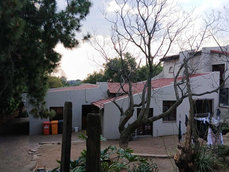 Rear view of the property featuring a multi-level structure with terracotta roof tiles, plastered walls, and a paved driveway area.