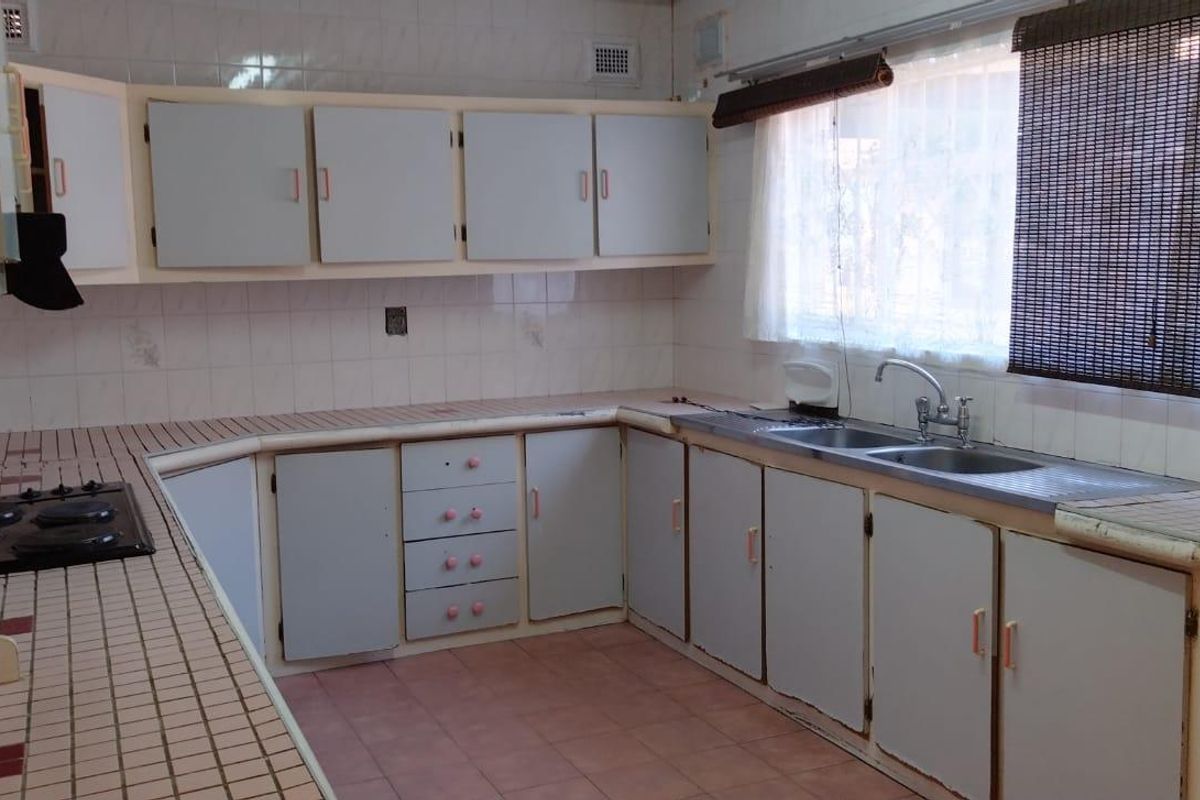 A dated kitchen featuring original cabinetry, tiled countertops, a built-in hob, and a double-basin sink with tiled flooring.