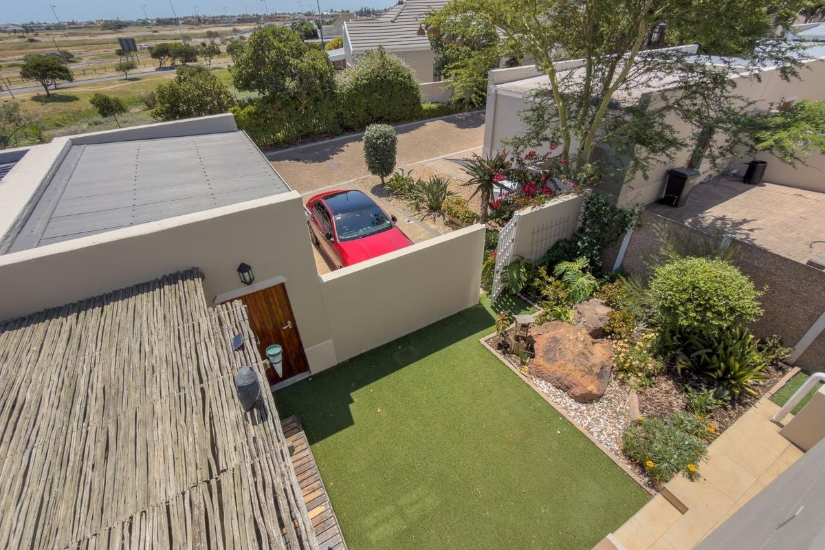 Aerial view of a residential property featuring a well-maintained artificial lawn, landscaped garden beds, and a thatched pergola area.